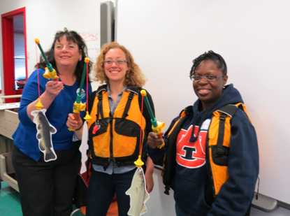 Three women holding kids fishing rods with paper fish on them.