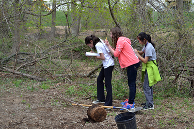 Teacher and students in a group putside looking at at book to identify a leaf.